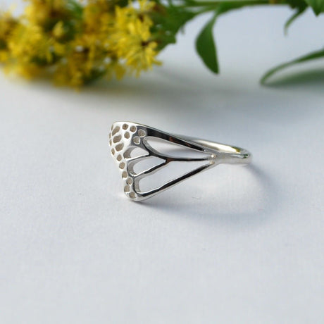 Bague aile de papillon monarque en argent posée sur fond blanc devant des fleurs de verge d'or jaunes, bijou inspiré du monarque de la marque québécoise Lasclay.
