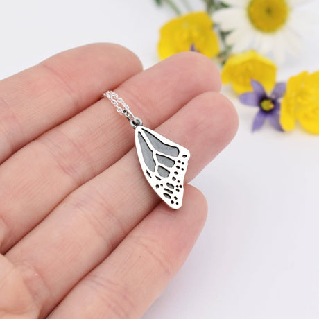 Pendentif aile de papillon monarque en argent posé sur une marguerite, nervures finement détaillées, sur fond blanc.
