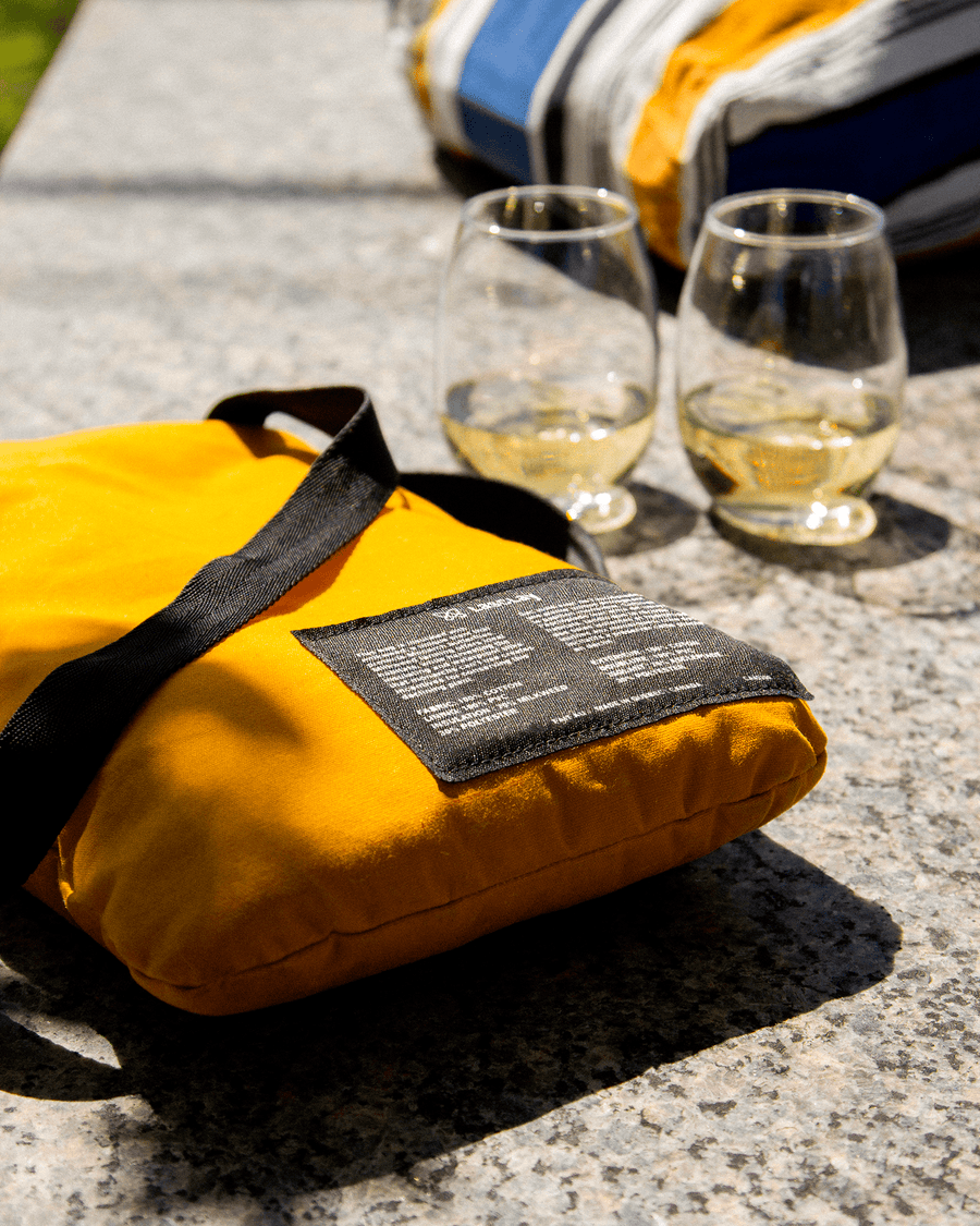 Sac fourre-tout isotherme jaune et deux verres de vin blanc posés sur une roche, scène de pique-nique ensoleillé