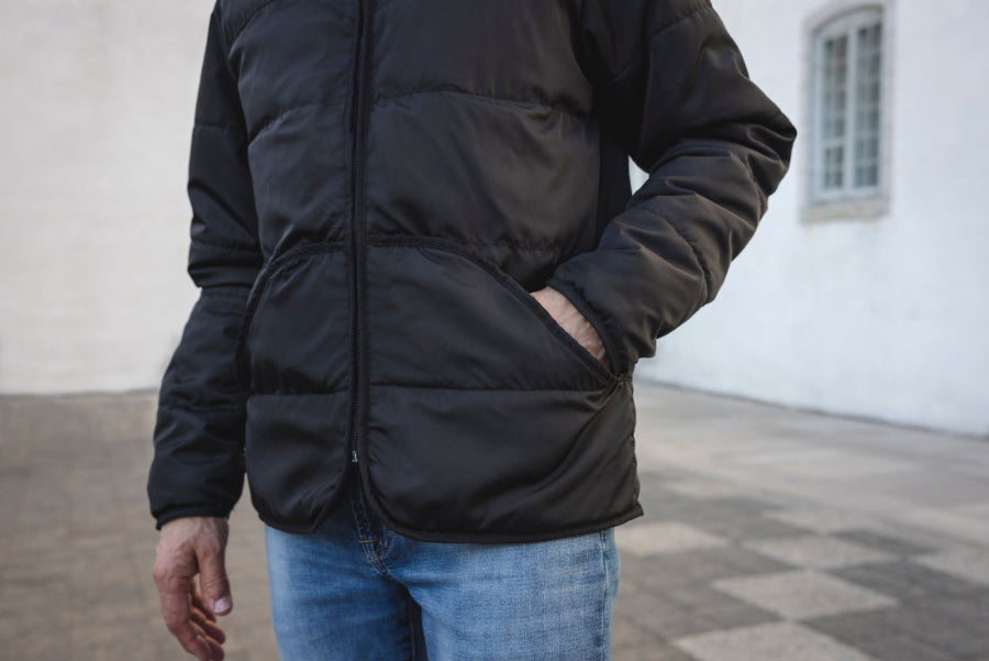 Homme portant un manteau Lasclay noir écologique isolé en asclépiade dans la cour ancestrale du Petit Séminaire de Québec