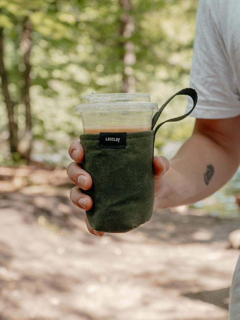 Manchon vert isolant pour café glacé tenu à la main – accessoire réutilisable en asclépiade, écoresponsable et pratique.